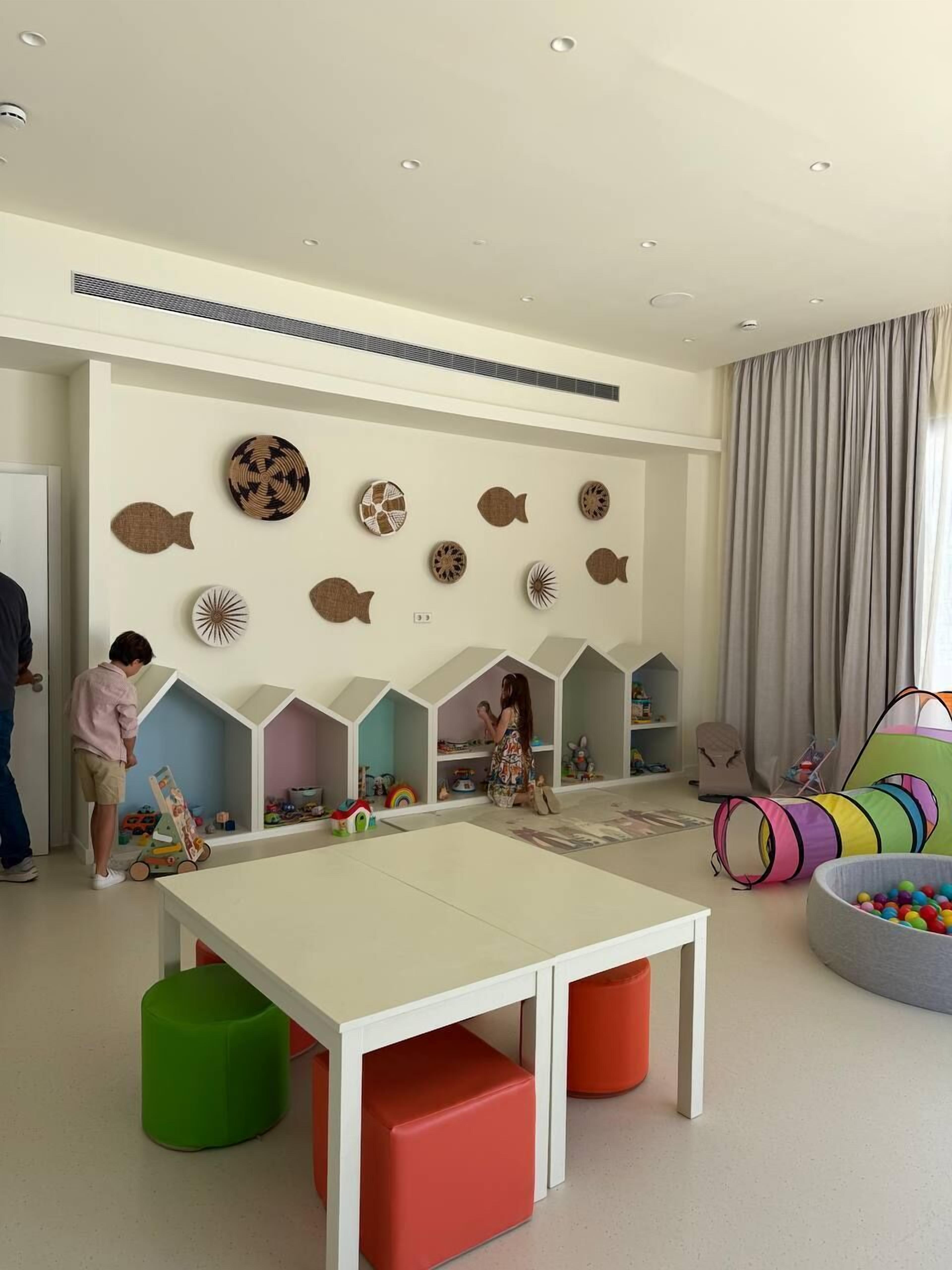 A children's playroom with a white table, colorful storage units, and a wall decorated with fish-themed wall art.