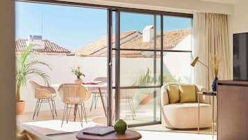 Un salon moderne doté d’une grande porte-fenêtre coulissante donnant sur un patio extérieur. L’intérieur comprend un canapé, une table basse ronde et des fauteuils en osier.