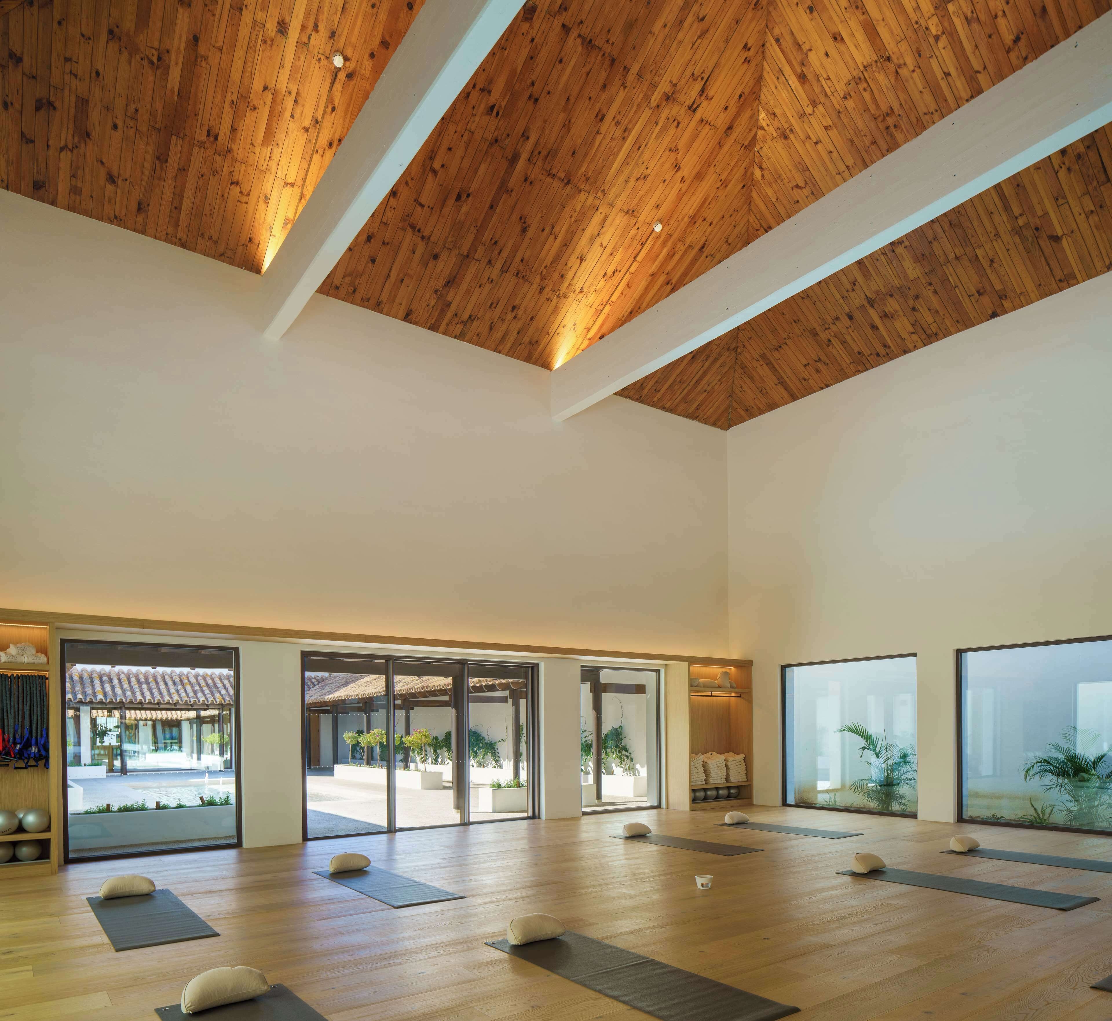 A spacious room with wooden flooring, large windows, and a high ceiling with wooden beams.