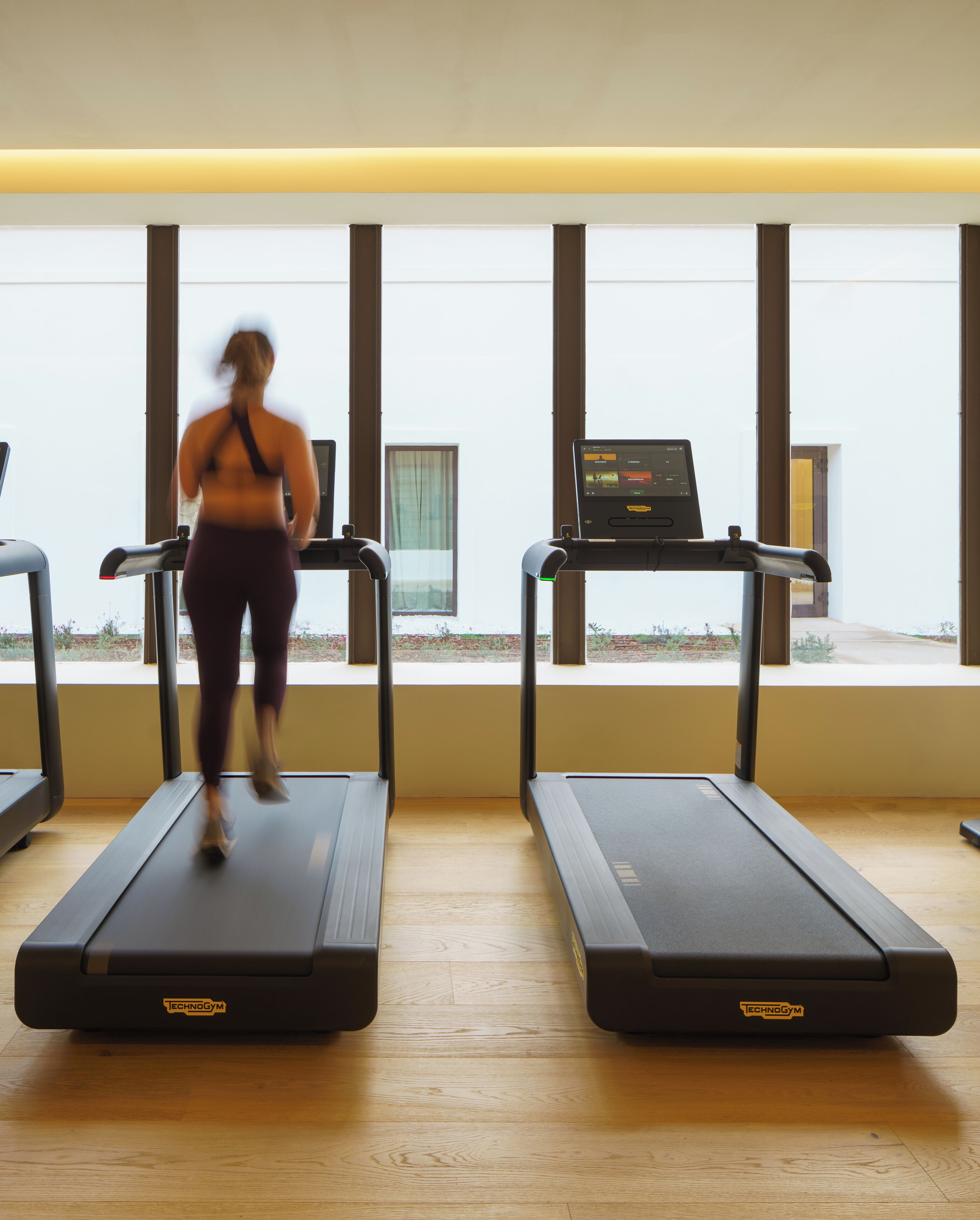 Un gimnasio con dos cintas de correr, un ventanal y vistas al exterior.