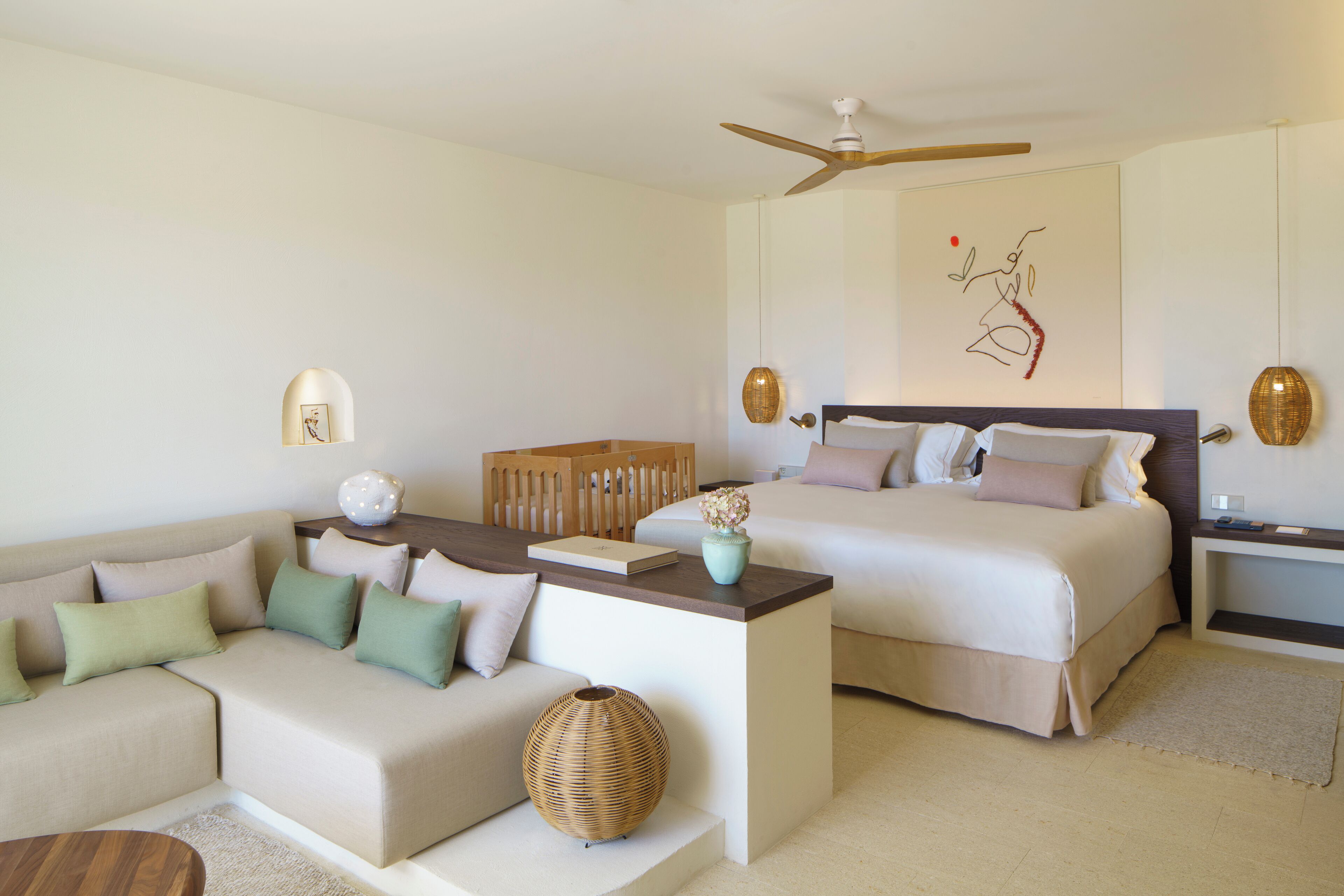 A hotel room with a sofa, two beds, a ceiling fan, and a wall art piece.