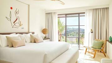 A spacious bedroom with a large bed, a ceiling fan, a view of the outdoors through a sliding glass door, and a wicker chair by the window.