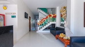 Uma área de recepção de hotel, com balcão, escada e sala de estar, incluindo sofás e mesa de centro.