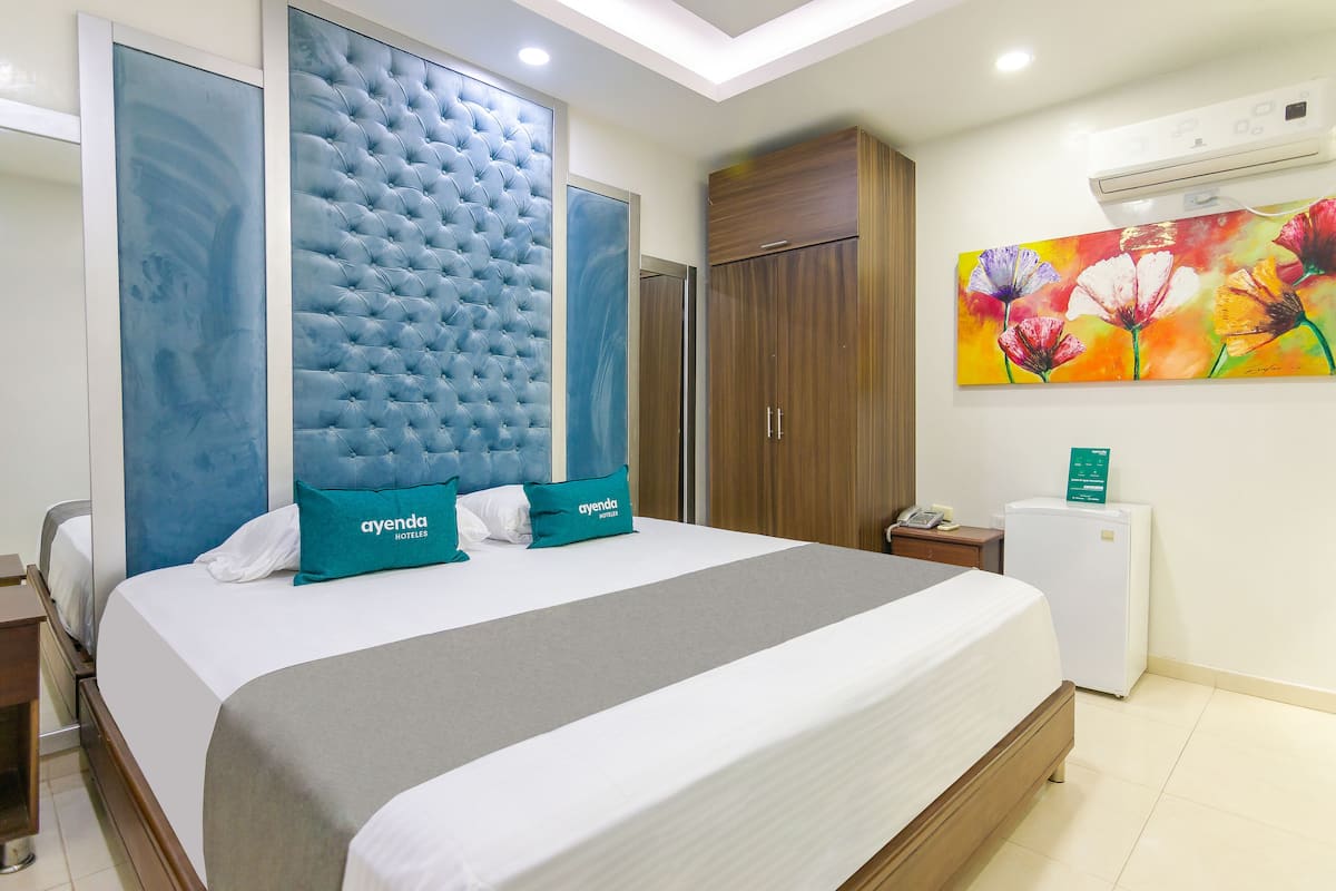 Una habitación de hotel con una cama grande, un armario, una mesita de noche, un escritorio y un refrigerador.