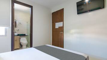 A hotel room with a bed, a wooden wardrobe, a toilet, and a TV mounted on the wall.