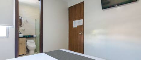 A hotel room with a bed, a wooden wardrobe, a toilet, and a TV mounted on the wall.