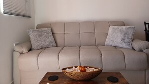 A beige sofa with two fluffy pillows, a wooden coffee table with a bowl of snacks, and a sunset painting on the wall. - D2 Stylish Brand New Apartment - Nuevo Apartamento (San Carlos)