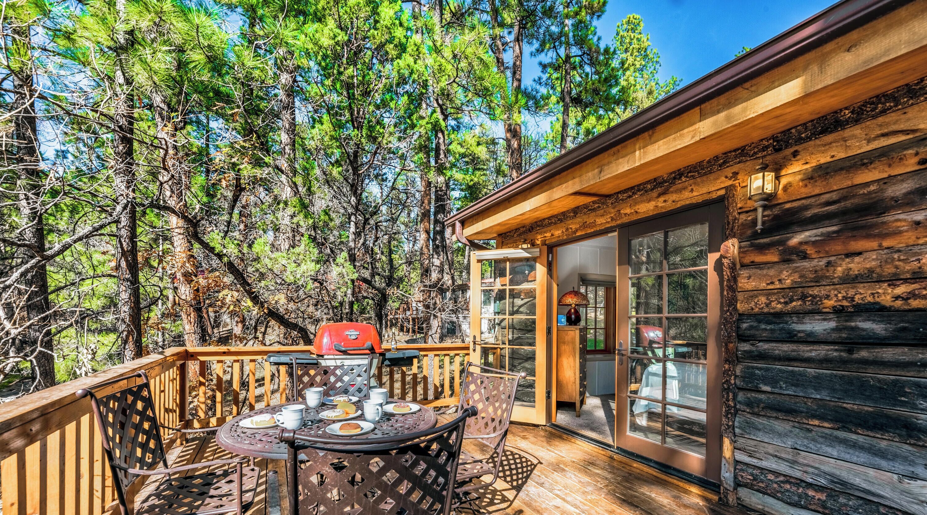 A wooden deck with a table and chairs, a grill, and a glass door leading to a cabin.