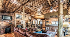 L’intérieur d’un chalet rustique, avec des murs en bois, un canapé en cuir, un coin repas et une cuisine.