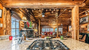 A rustic cabin interior with a stone fireplace, wooden ceiling beams, a large kitchen area with a gas stove, and a cozy seating area with a fireplace. - The Apple Tree | Tranquil Rio Ruidoso Cabin w/ Deck Views, River Sounds & Cozy Charm (Ruidoso)