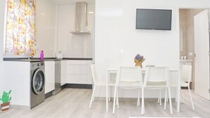A modern kitchen with a washing machine, a dining area with white chairs, and a flat-screen TV mounted on the wall. - Chalet del Sultan with pool and WiFI (Conil de la Frontera)
