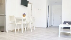A modern, minimalist dining area with a white table and chairs, a flat-screen TV mounted on the wall, and a hallway leading to another room. - Chalet del Sultan with pool and WiFI (Conil de la Frontera)