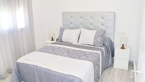 A bedroom with a tufted headboard, a bed with patterned bedding, two bedside tables with lamps, and a window with sheer curtains. - Chalet del Sultan with pool and WiFI (Conil de la Frontera)