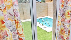 A swimming pool with a metal ladder, surrounded by a green lawn and beige walls. - Chalet del Sultan with pool and WiFI (Conil de la Frontera)