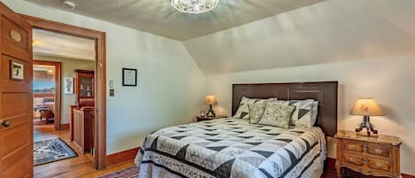 A bedroom with a large bed, two bedside tables with lamps, a wooden door, and a patterned rug.