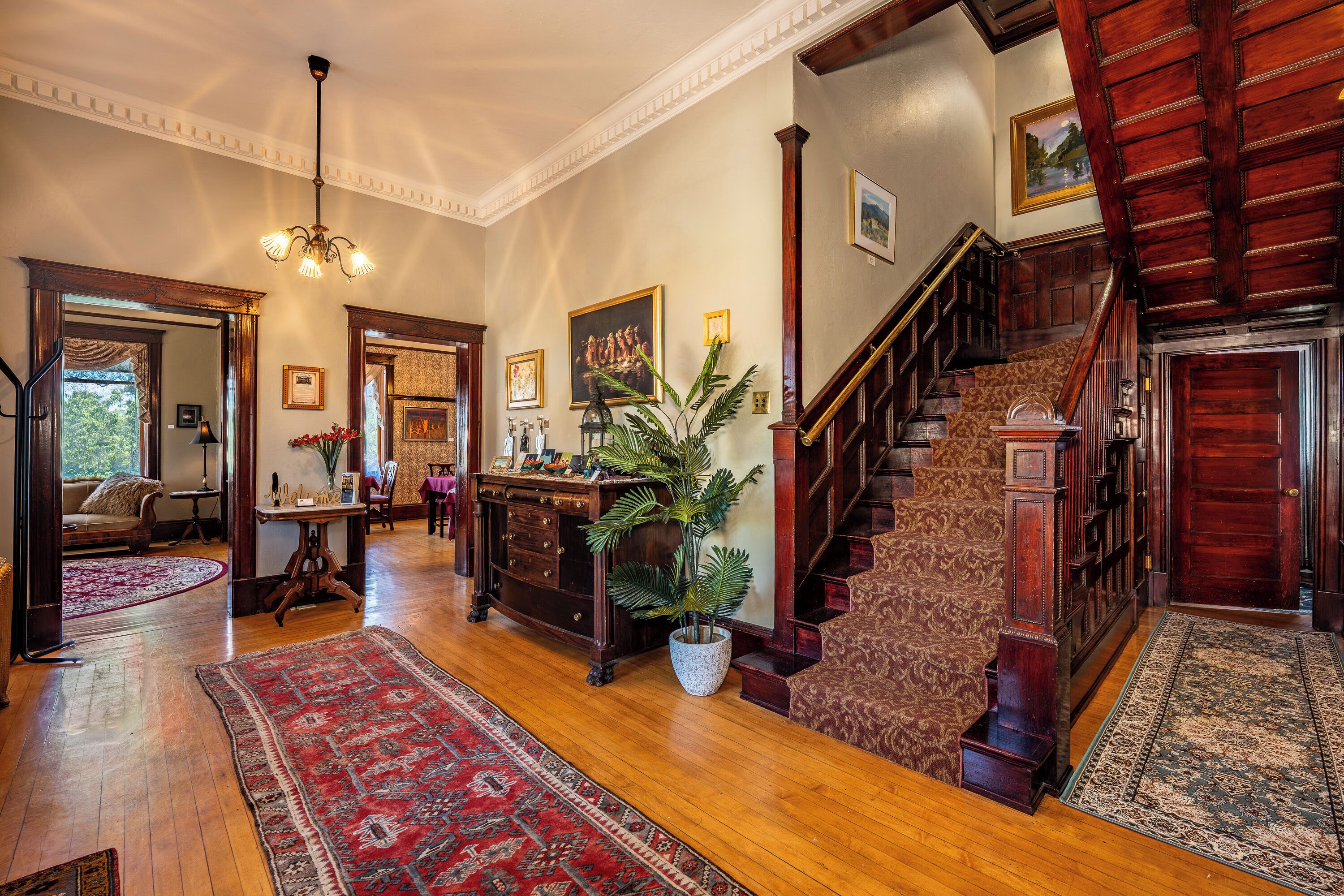 A spacious foyer with a grand staircase, wooden flooring, and a large potted plant.