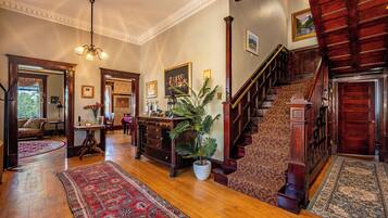 A spacious foyer with a grand staircase, wooden flooring, and a large potted plant.