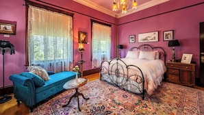 A room with a bed, a blue sofa, a chandelier, and a large window with curtains.