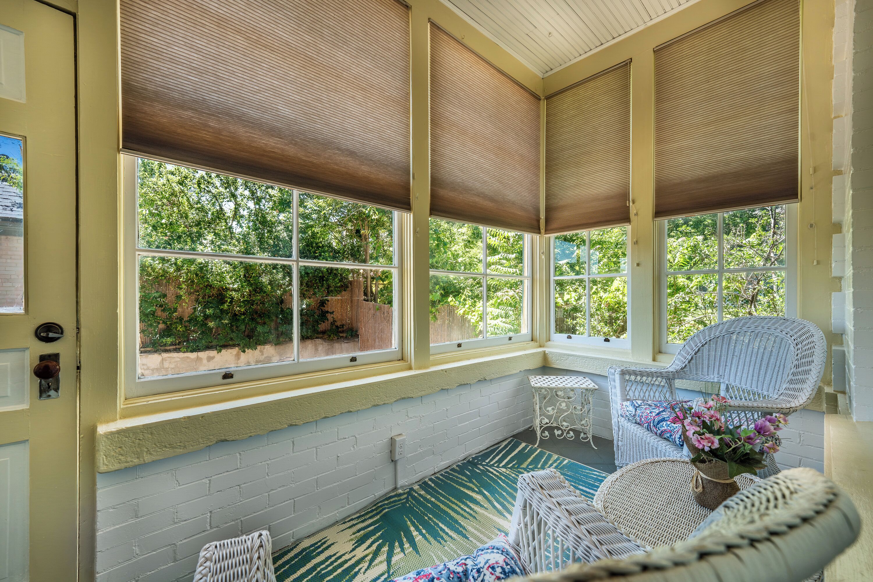 A sunroom with large windows, wicker furniture, and a view of greenery outside.