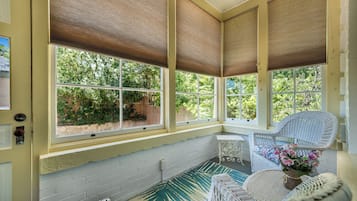 A sunroom with large windows, wicker furniture, and a view of greenery outside.