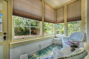 Una sala de estar con ventanales amplios, muebles de mimbre y vistas al verdor exterior.
