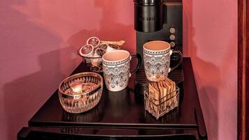 A coffee maker, two patterned mugs, a bowl of snacks, and a candle on a table.