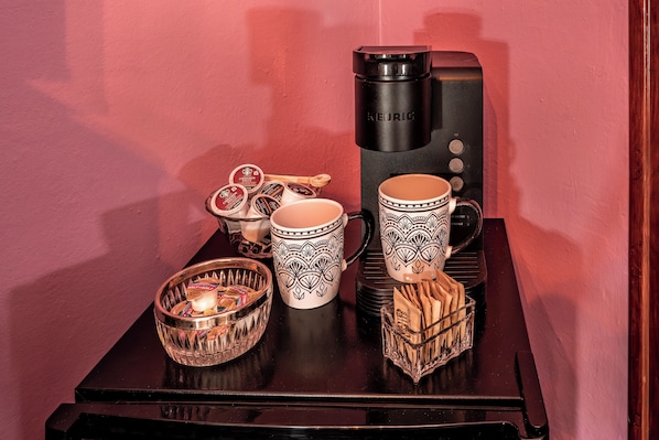 A coffee maker, two patterned mugs, a bowl of snacks, and a candle on a table. - Tarabino Inn (Trinidad)