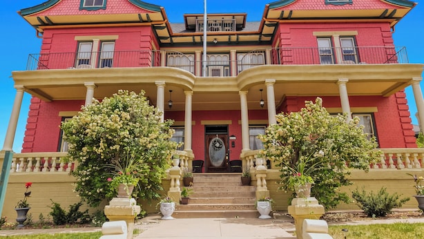 A two-story red house with a balcony, a front porch, and steps leading to the entrance.