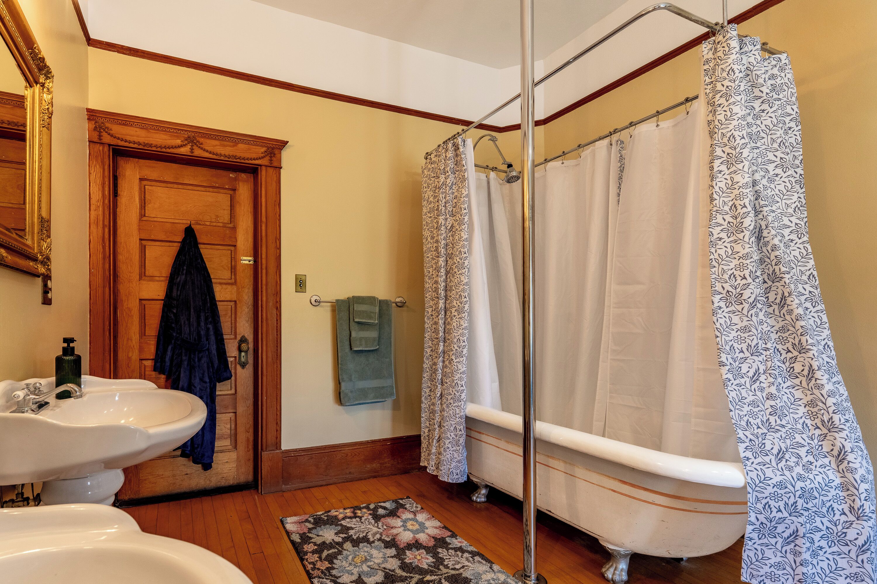 Un baño con dos lavamanos, una bañera, un cortinón de ducha y una puerta de madera.