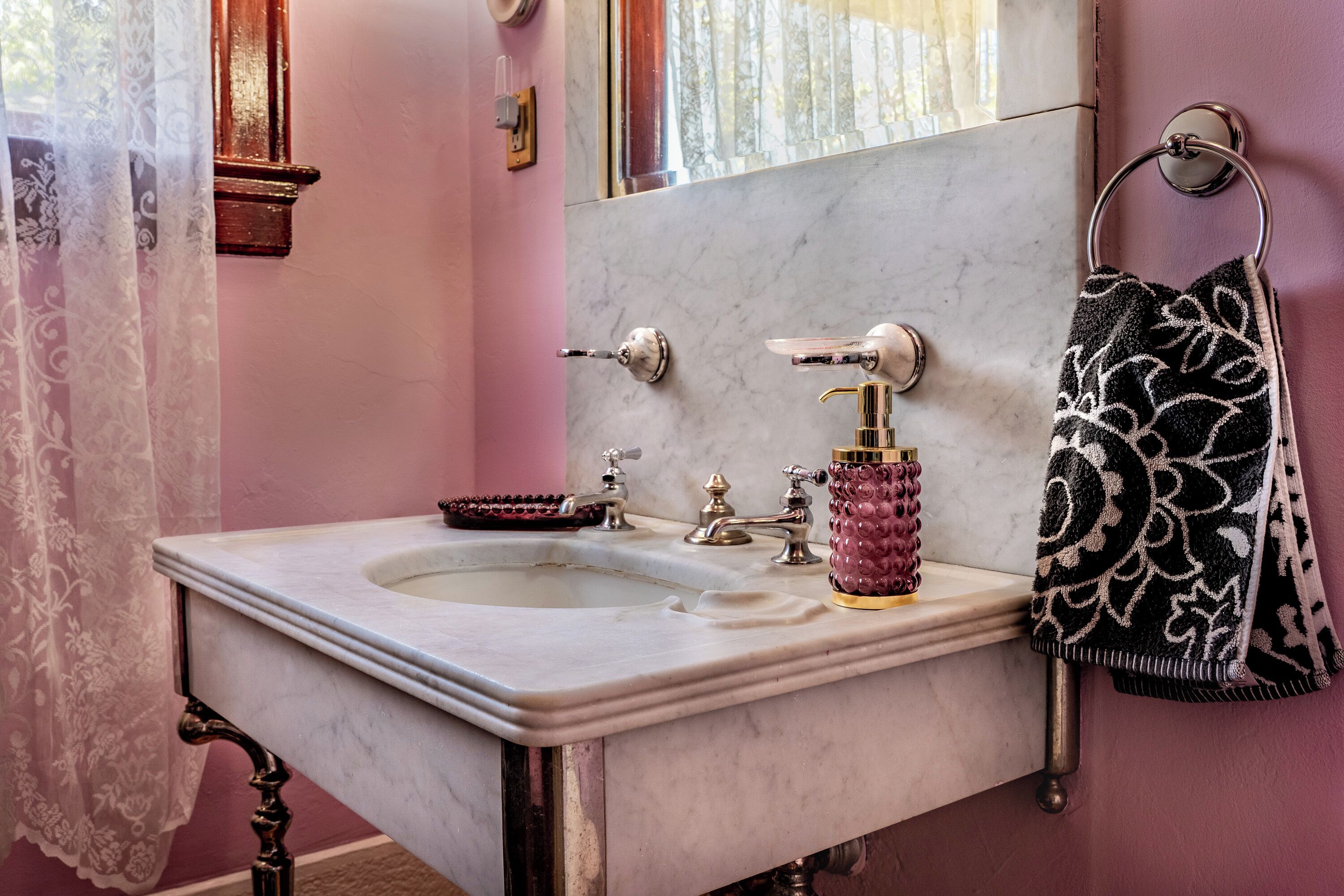 Un baño con lavamanos de mármol, espejo, toallero y un jarrón decorativo.