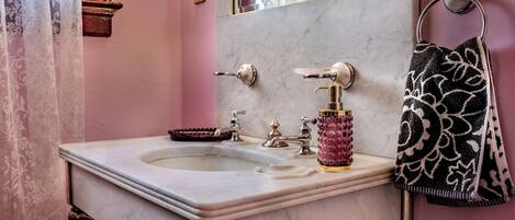 Un baño con lavamanos de mármol, espejo, toallero y un jarrón decorativo.