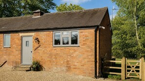 A brick house with a grey door, a window with a white frame, and a wooden gate. - Paddock Cottage - sleeps 2 guests in 1 bedroom (Winchcombe)