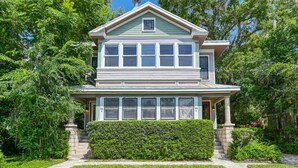 A two-story house with a covered porch, a well-maintained lawn, and a stone staircase leading to the entrance. - Walk to Historic District & Shops, Close to Beach, Free Driveway Parking, $300 in Free Tickets! (St. Augustine)