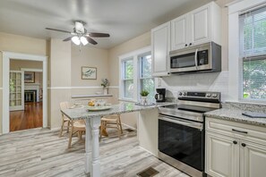 A modern kitchen with white cabinetry, a granite countertop, a built-in microwave, a double oven, and a ceiling fan.