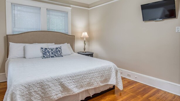 A bedroom with a bed, a nightstand, a lamp, a television, and a window with blinds. - Walk to Historic District & Shops, Close to Beach, Free Driveway Parking, $300 in Free Tickets! (St. Augustine)