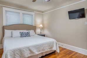 A bedroom with a bed, a nightstand, a lamp, a television, and a window with blinds.