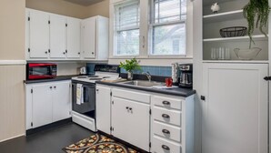 A kitchen with white cabinets, a red microwave, a stove, a sink, and a window with blinds. - Walk to Historic District & Shops, Close to Beach, Free Driveway Parking, $300 in Free Tickets! (St. Augustine)