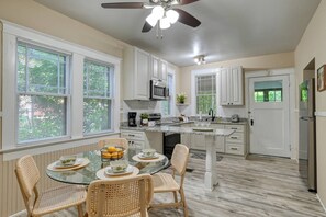 A kitchen with white cabinets, a microwave, a coffee maker, and a dining area with wicker chairs and a glass table.