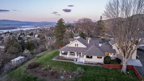 A residential house with a large front yard, a patio, and a view of a river and mountains in the background. - Expansive Panoramic View of Columbia Gorge, Enormous Deck and Seating, BBQ, Billiards, Darts, Games (The Dalles)