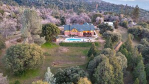 A large house with a swimming pool, surrounded by trees and hills.