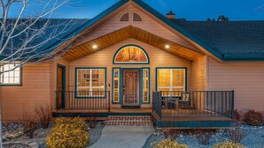 A two-story log cabin with a porch, a wooden front door, and a small deck.
