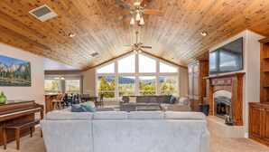 A spacious living room with a large sectional sofa, a wooden ceiling with a fan, a fireplace, and a television.