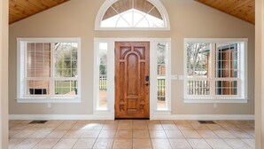 A spacious entryway with a wooden ceiling, a large wooden door, and two windows on either side.