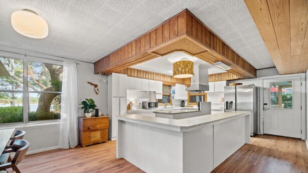 Una cocina moderna con detalles de madera, una isla central y ventanas amplias con vistas al exterior.