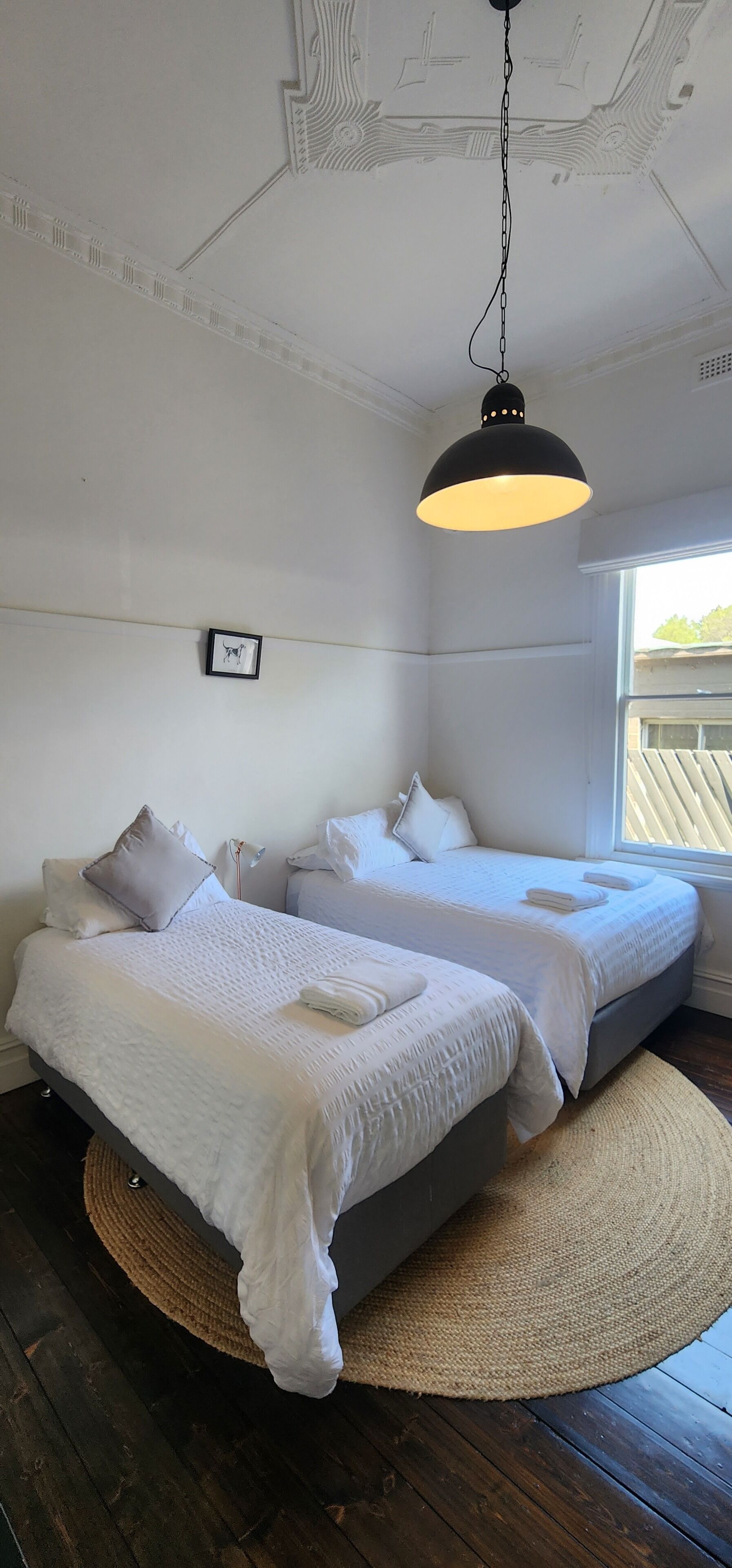 A bedroom with two beds, a hanging light fixture, and a window.