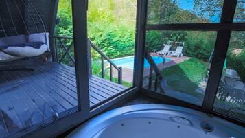 A hot tub with a view of a swimming pool and outdoor seating area.
