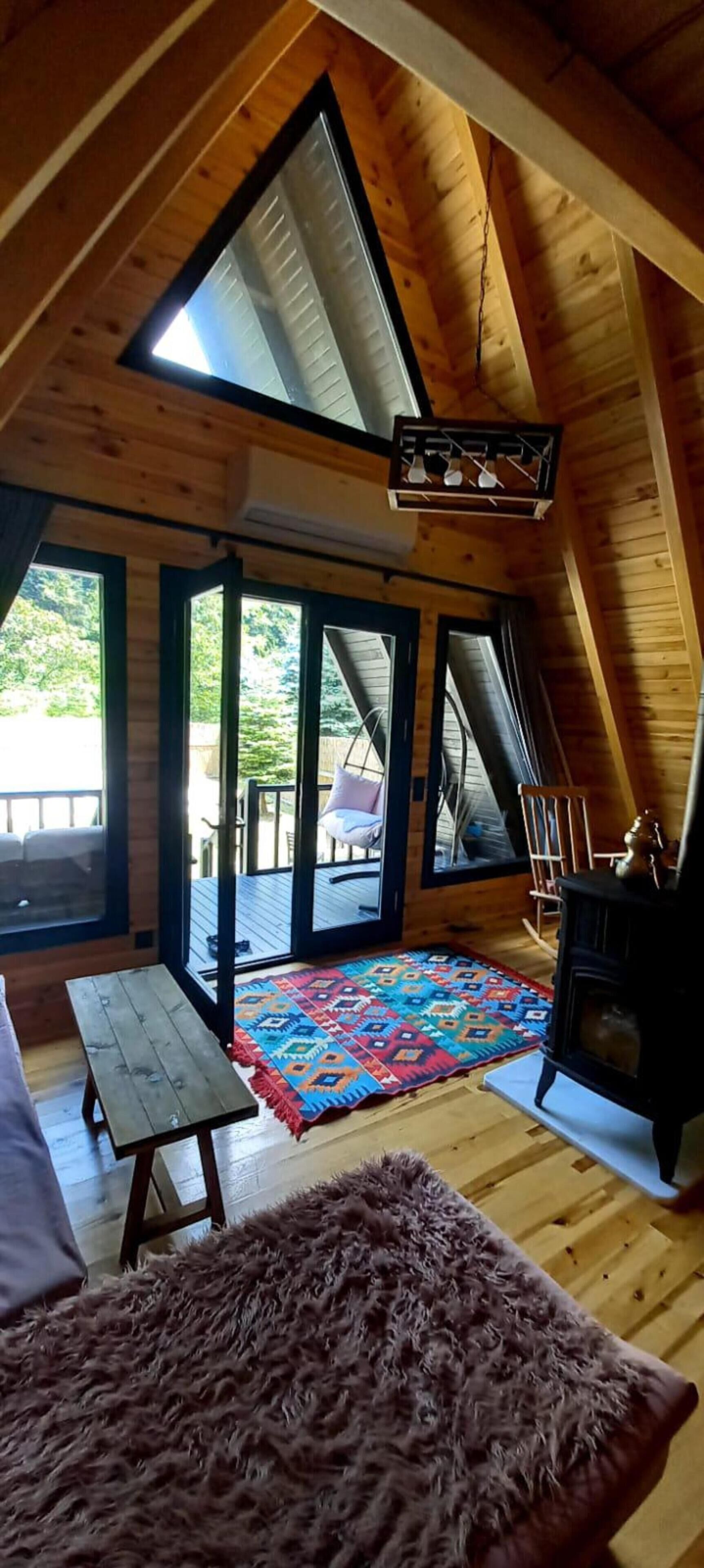 A wooden interior with a lofted ceiling, a fireplace, a bench, and a colorful rug.