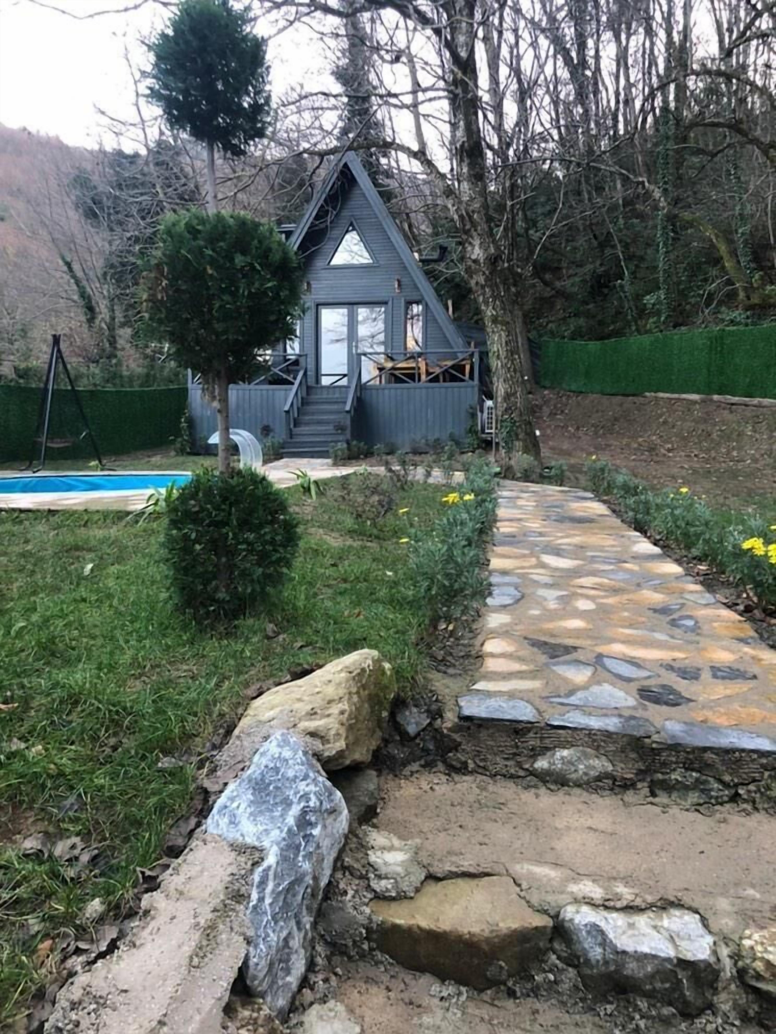 Une petite maison moderne avec un chemin de pierre menant à une piscine.