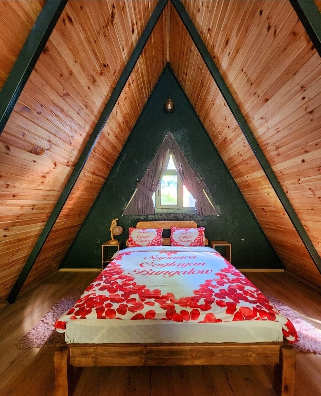 Ein gemütliches Schlafzimmer im Dachgeschoss mit schrägem Holzboden, einem Bett mit zartem Rosenmuster auf der Bettwäsche und einem Fenster mit Vorhängen.