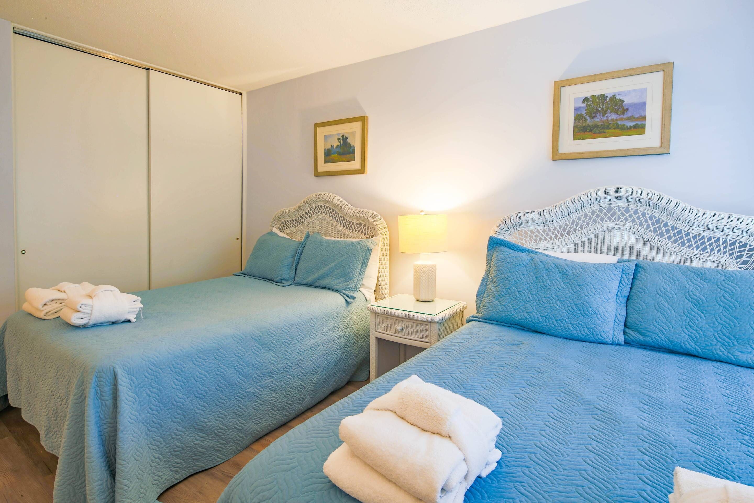 A bedroom with two beds, a nightstand with a lamp, and a wardrobe.